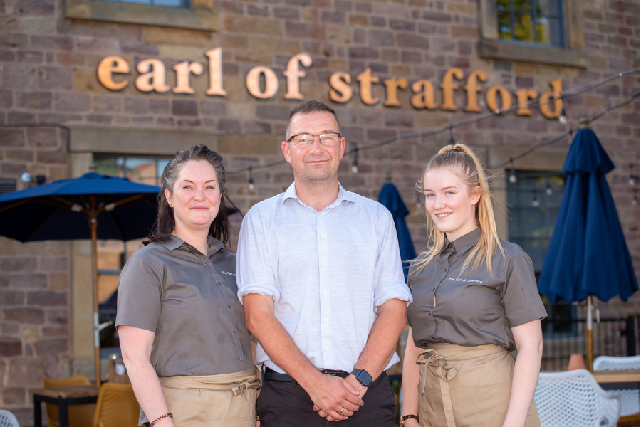 2 female team members and manager in front of Earl of Strafford sign.